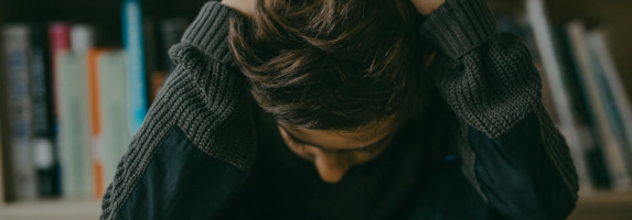 Weiterbildung Traumapädagogik Ein Kind sitzt in einer Bücherei auf dem Boden und hat die Arme über dem Kopf verschränkt und blickt nach unten