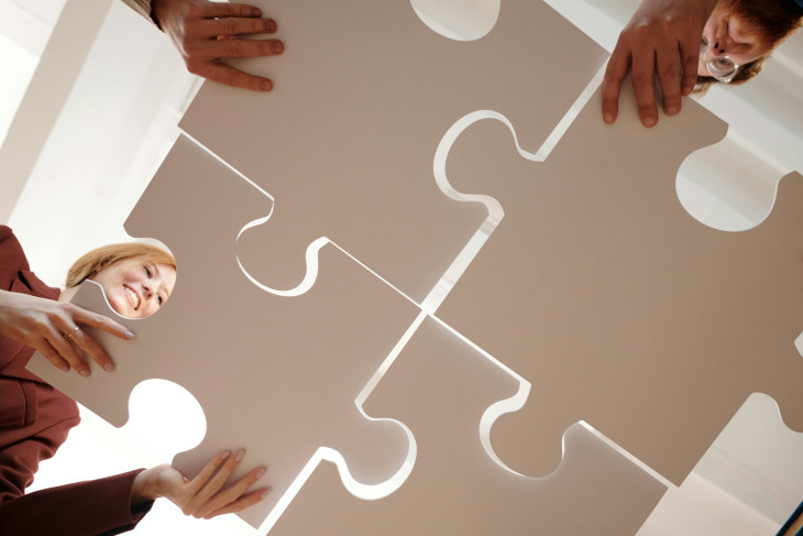 Ein Foto zeigt von unten wie große Puzzleteile von Personen zusammengehalten werden